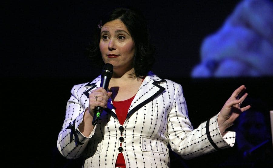 Alex Borstein holding a microphone on stage