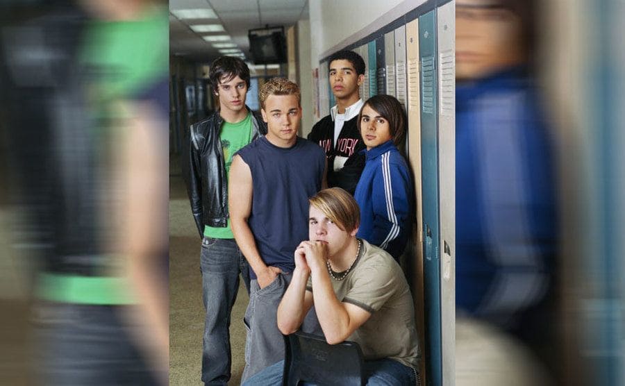 Some of the cast of Degrassi posing with Drake next to lockers in a high school hallway