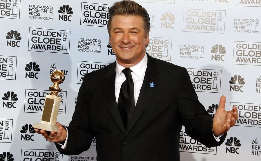 Alex Baldwin holding a Golden Globe Award on the red carpet for his performance in 30 Rock