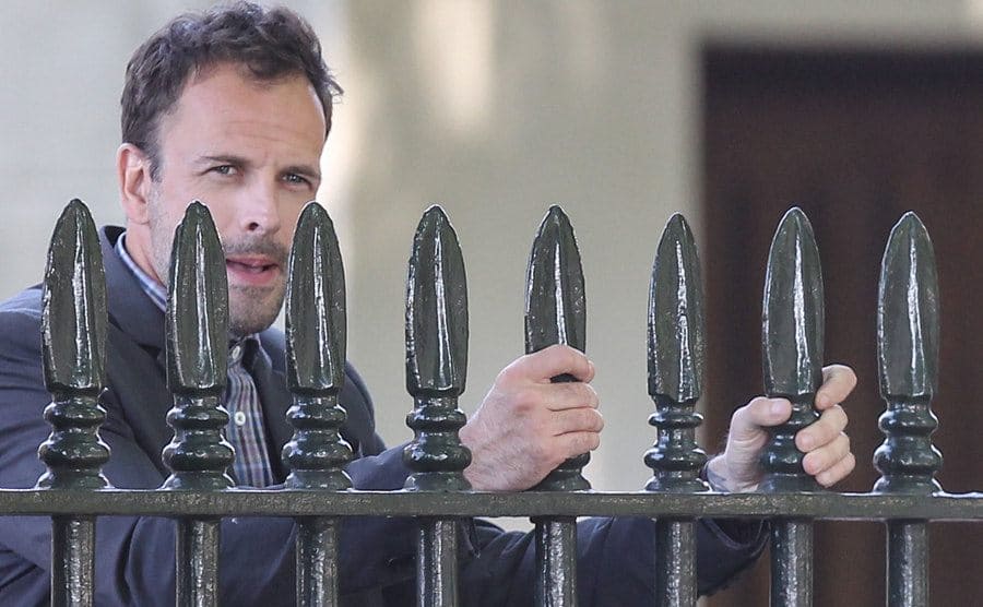 Jonny Lee Miller behind a large black metal gate while filming a scene from Elementary