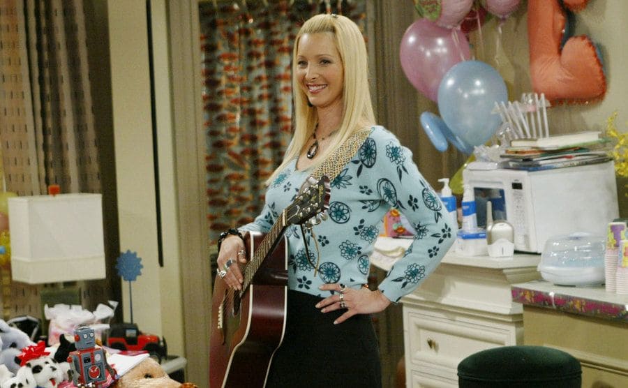 Lisa Kudrow holding her guitar in the kitchen of Joey’s apartment
