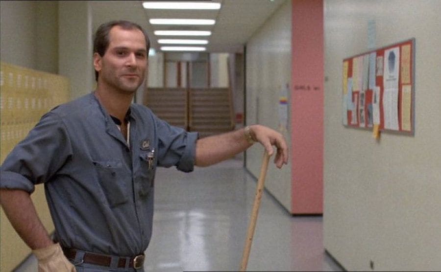 John Kapelos as Carl the Janitor leaning on a mop handle in a school hallway in The Breakfast Club