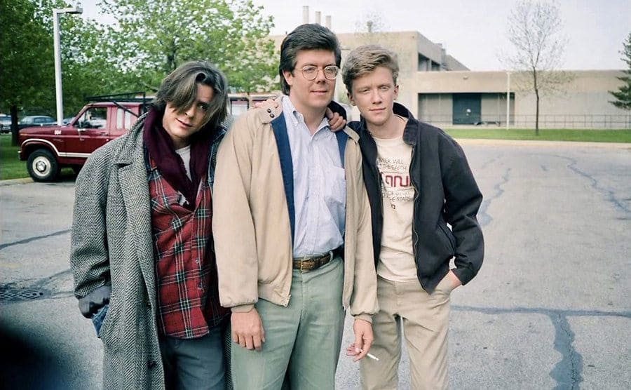 Judd Nelson, John Hughes, and Anthony Michael Hall posing together in the school parking lot during the shooting