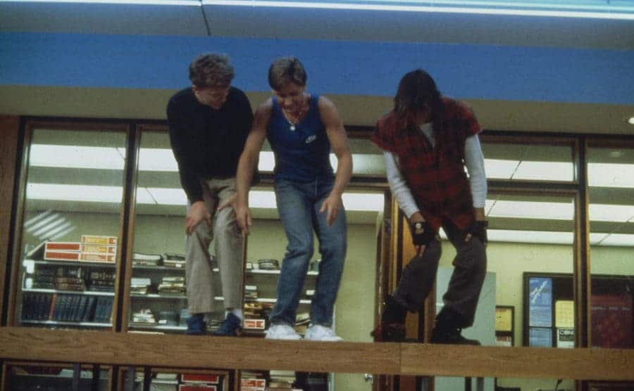 Emilio Estevez, Anthony Michael Hall, and Judd Nelson dancing together in the library at a table
