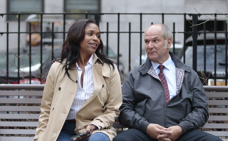 John Kapelos sitting on a park bench with Merrin Dungety in a scene from Conviction