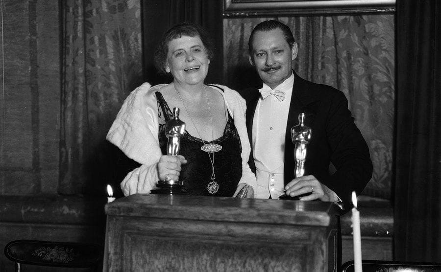 Marie Dressler and Lionel Barrymore holding their Oscars behind a podium