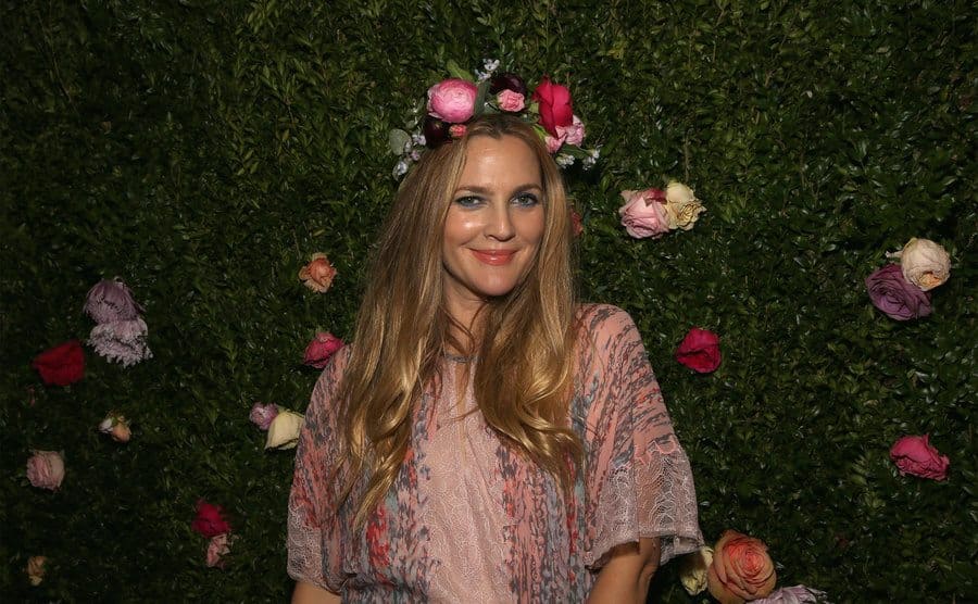 Drew Barrymore on the red carpet posing in front of a green leaf background