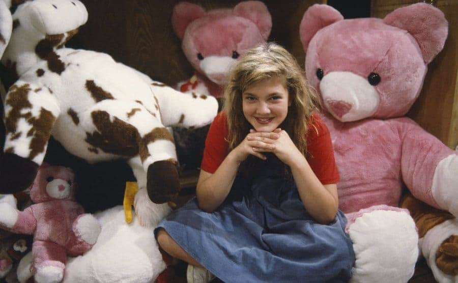 Drew Barrymore posing in front of stuffed animals with her chin resting on her hands