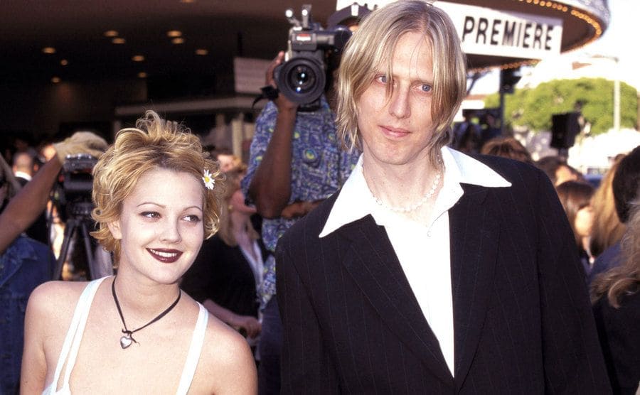 Eric Erlandson and Drew Barrymore holding hands on the red carpet of a film premiere