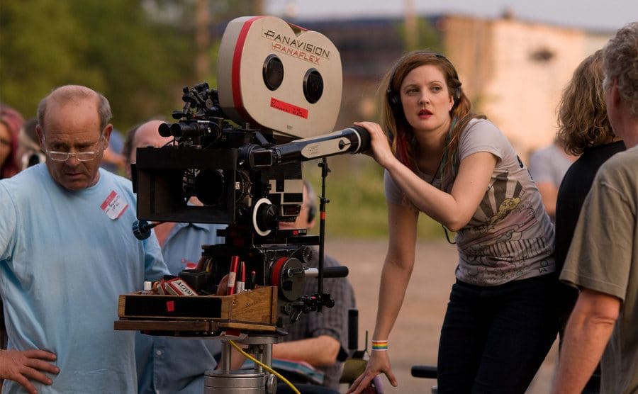 Drew Barrymore standing behind a video camera with headphones on the set of Whip It