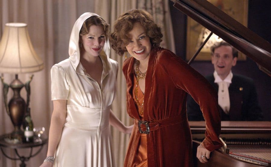 Drew Barrymore and Jessica Lange standing by a piano with a man sitting behind it