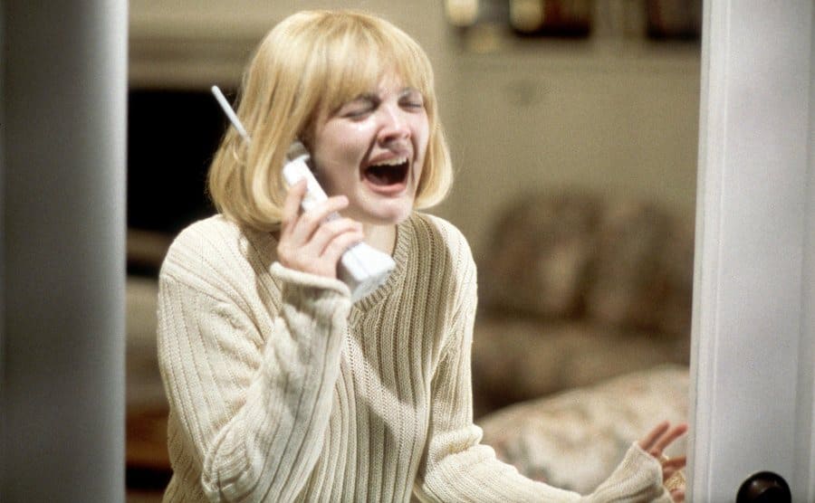Drew Barrymore screaming into a phone while standing by a glass door