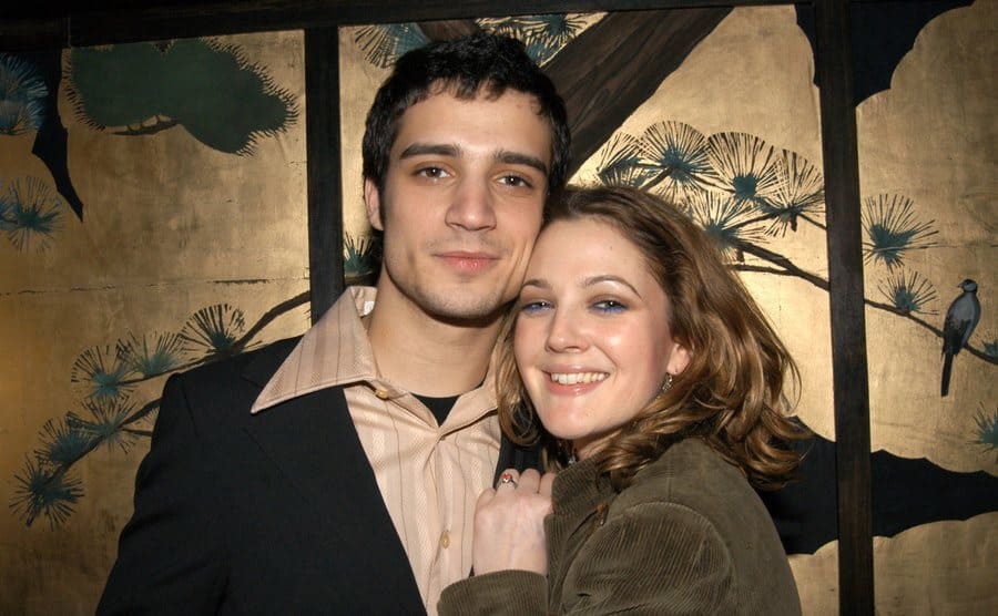 Fabrizio Moretti and Drew Barrymore posing in front of gold patterned wallpaper