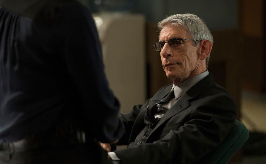 Richard Belzer as John Munch sitting behind a desk
