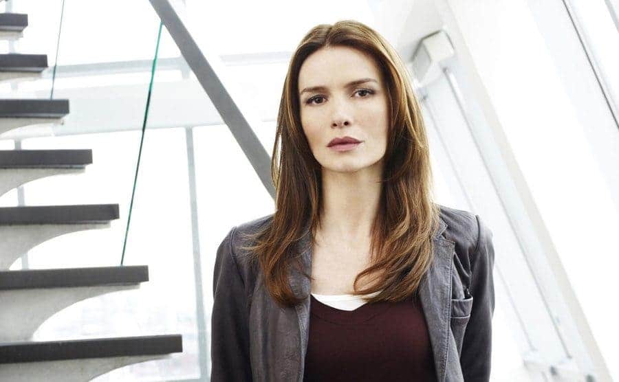 Saffron Burrows as Serena Stevens standing by a staircase