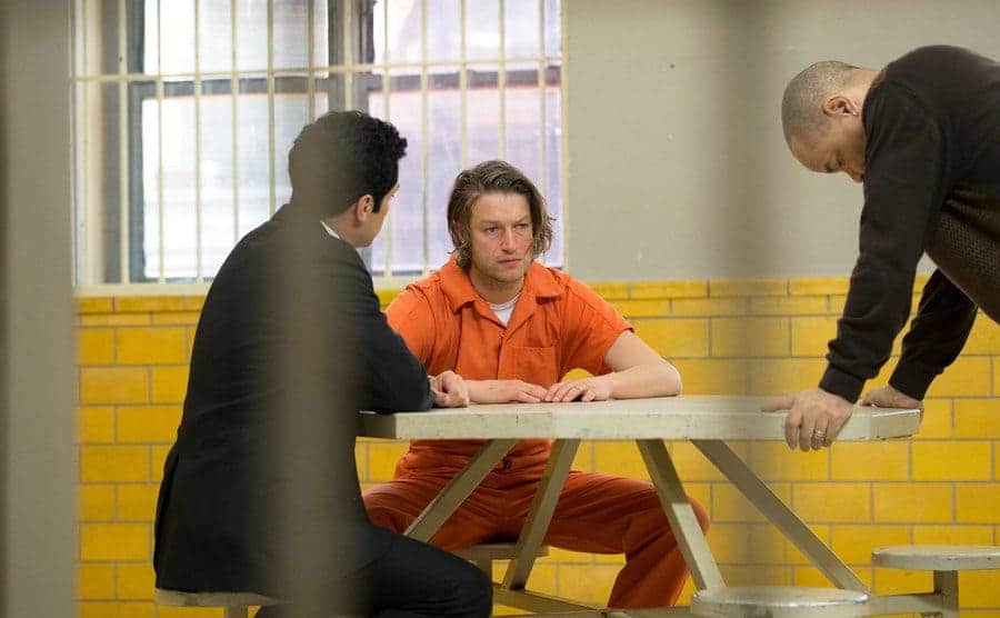 Peter Scanavino guest-starring sitting in an orange jumpsuit being interrogated in a scene from Law and Order