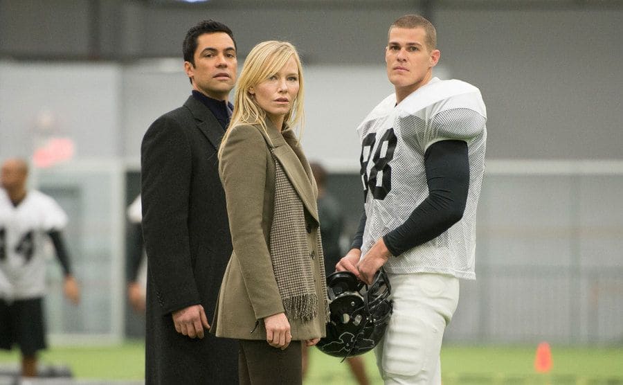 Danny Pino, Kelly Giddish, and Greg Finley on the football field in an episode of Law and Order