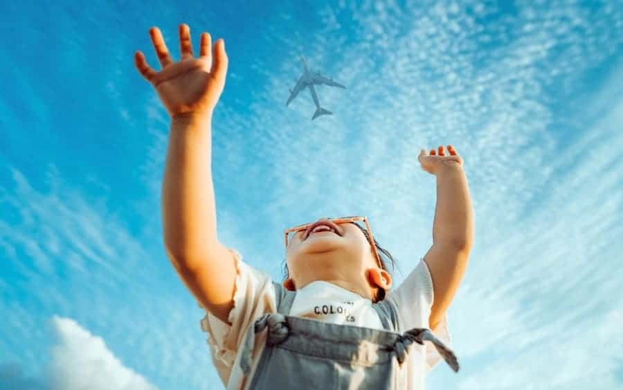 Little girl smiling and raised her hands waving to the airplane in the clear blue sky
