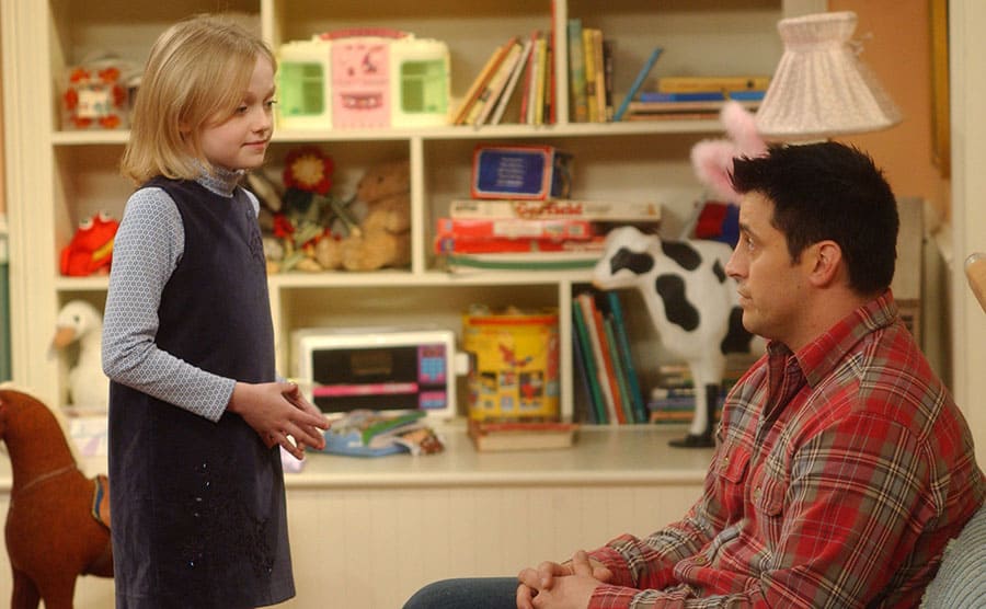 Dakota Fanning talking to Matt LeBlanc who is sitting in a small chair in her bedroom 
