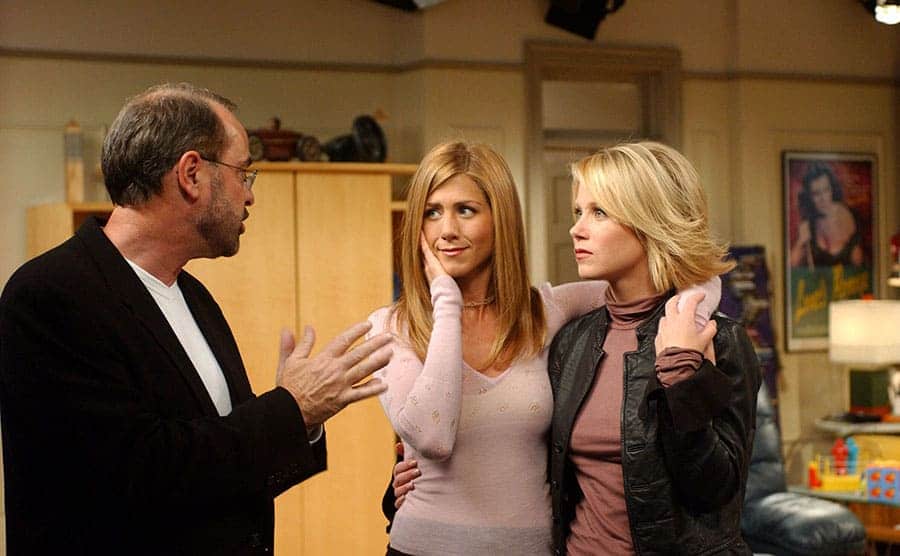 Jennifer Aniston and Christina Applegate with their arms around each other talking to a man 