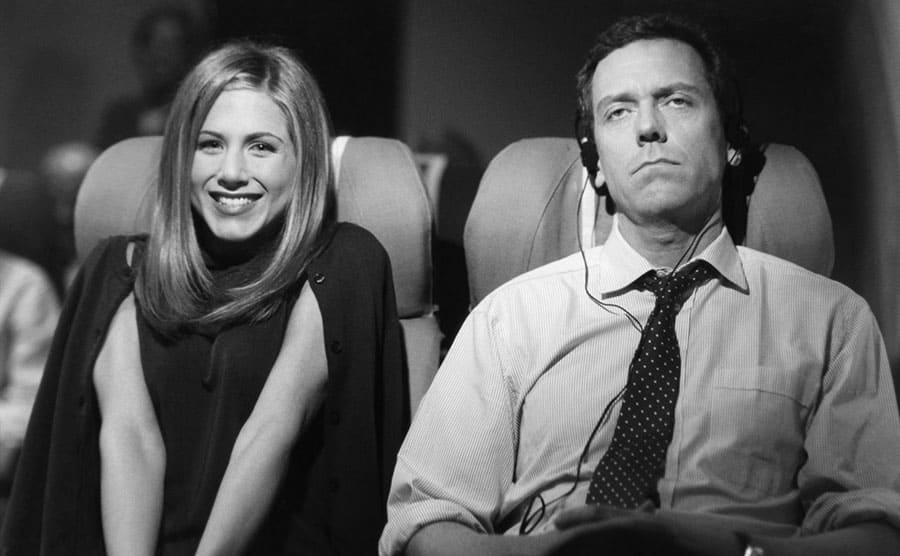 Jennifer Aniston and Hugh Laurie sitting on a plane in a scene from Friends 