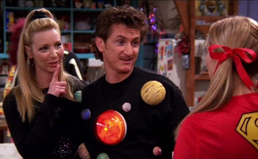 Lisa Kudrow standing with Sean Penn talking to a blonde girl dressed as Superwoman 