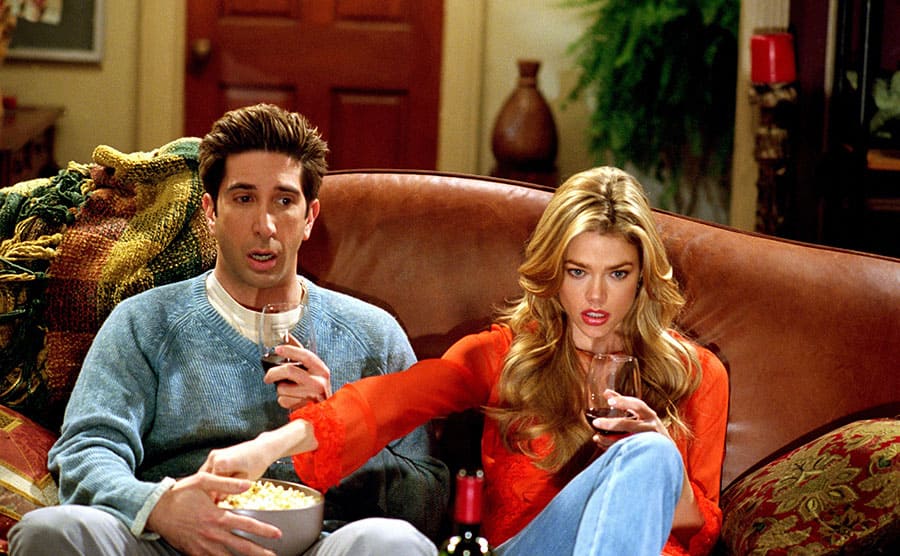 Denise Richards reaching into the popcorn bowl sitting on David Schwimmer’s lap while they are watching a movie 