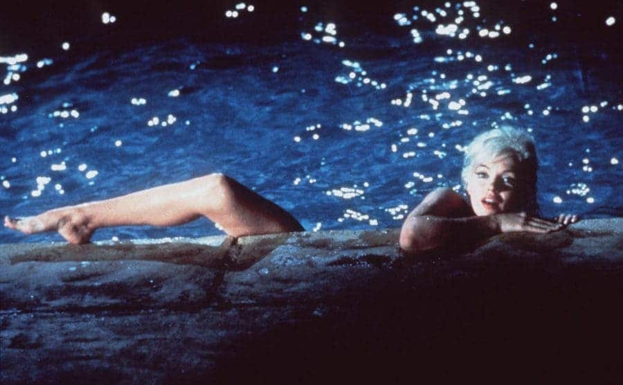 Marilyn Monroe with her foot and upper body coming over the edge of a swimming pool at night
