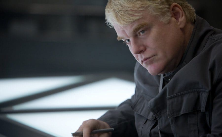 Philip Seymour Hoffman sitting at a table in The Hunger Games