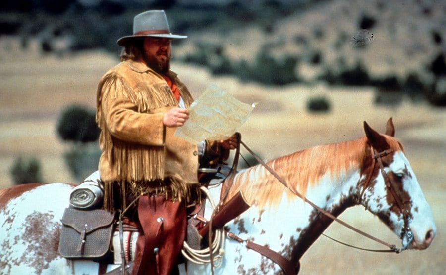 John Candy reading a map while sitting on a horse
