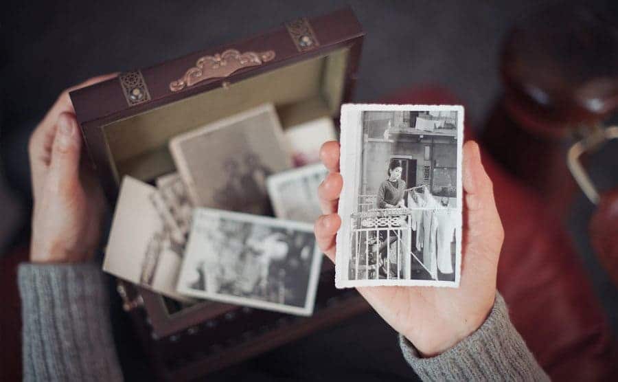 Hands of a woman discovering a treasure chest full of photographs and holding an old black and white photograph.