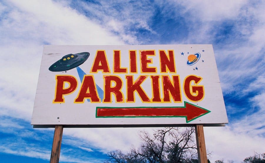 This is a road sign indicating where Alien Parking is, This is the original UFO crash site in Roswell, There are small UFOs on the sign with a large arrow pointing to the right.