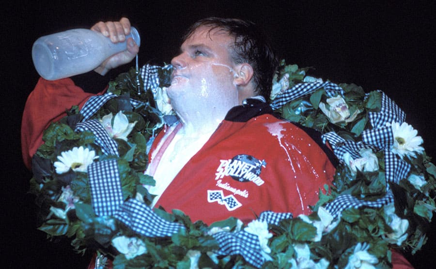 Chris Farley pouring milk over his face while he wears a floral wreath