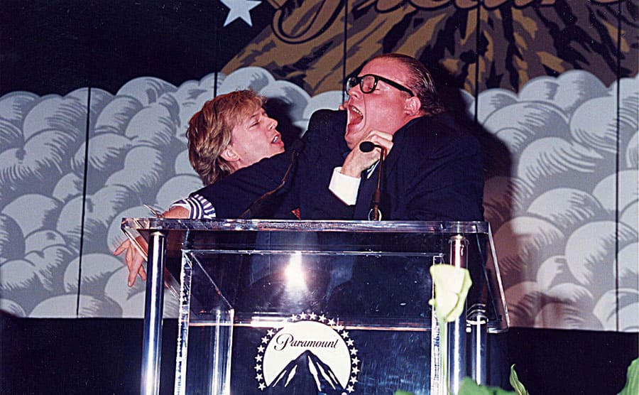 David Spade and Chris Farley pretending to argue over a microphone on stage