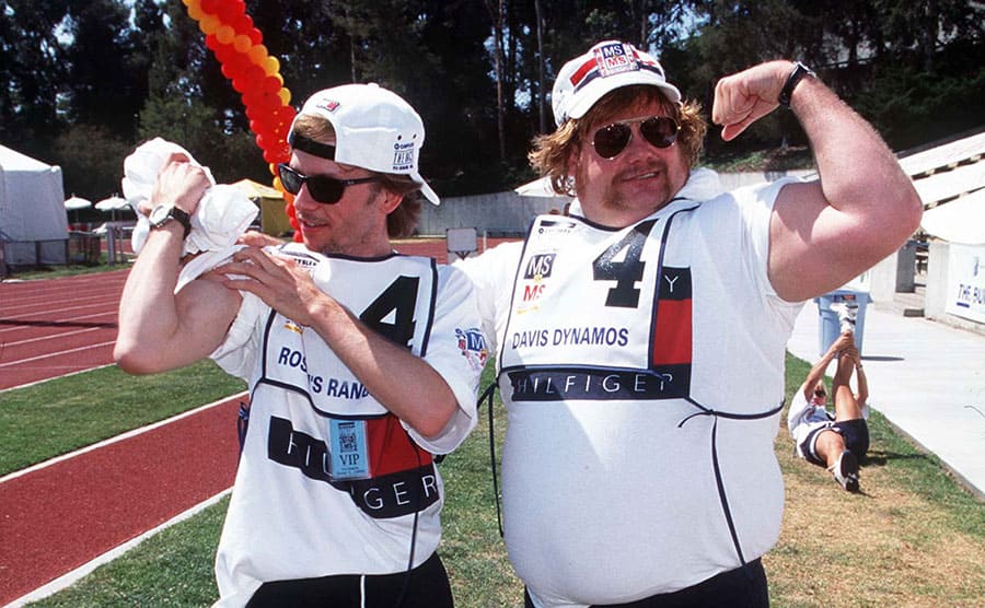 Chris Farley and David Spade looking at their arm muscles