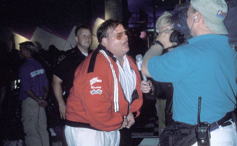 Chris Farley acting intoxicated in front of the press while an officer stands by
