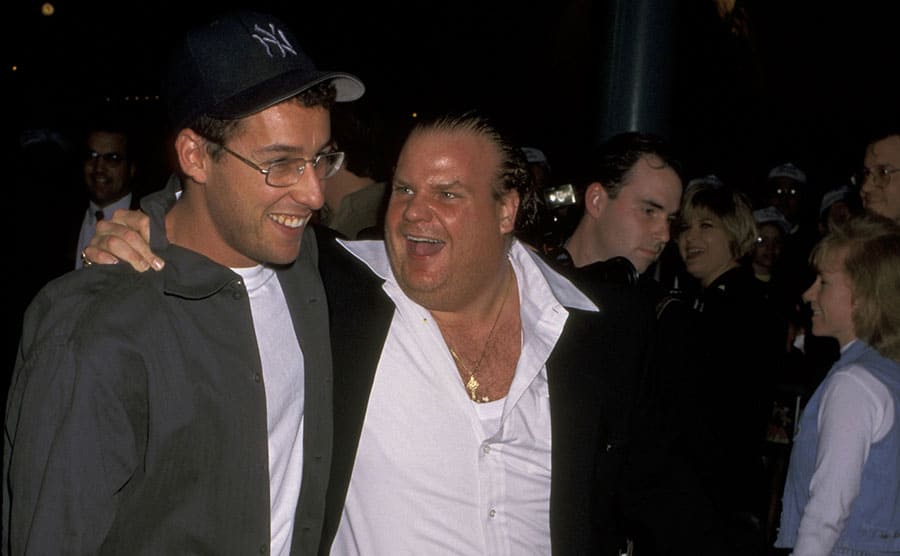 Chris Farley walking with his arm around Adam Sandler while talking