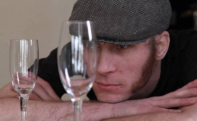 Josh is resting his face on a table covered with champaign flutes.