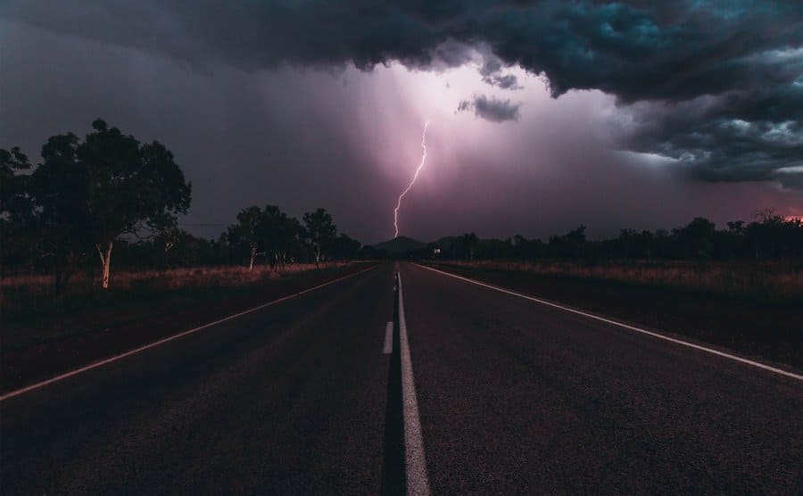 Looking down a road to a distant storm and lightning bolt. 