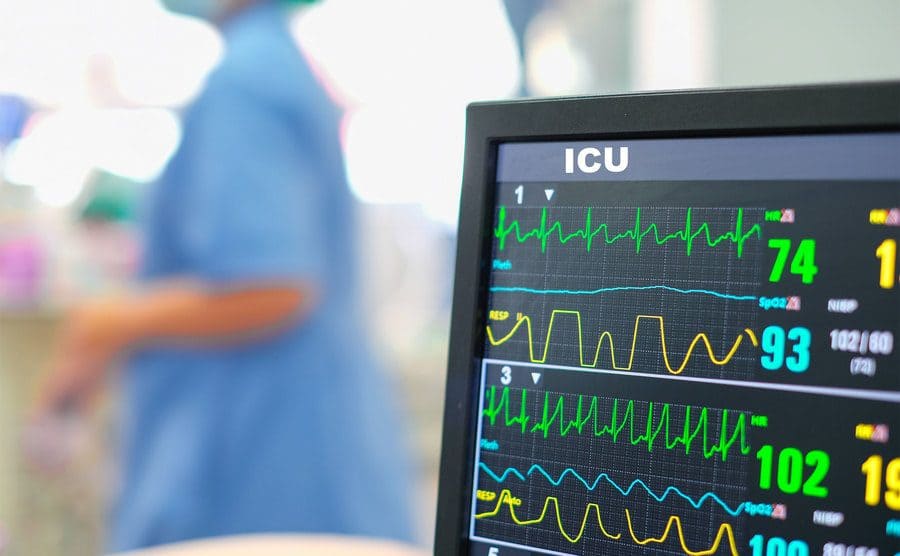 Heart rate monitor, patient and doctors in the background in intensive care unit or emergency room.