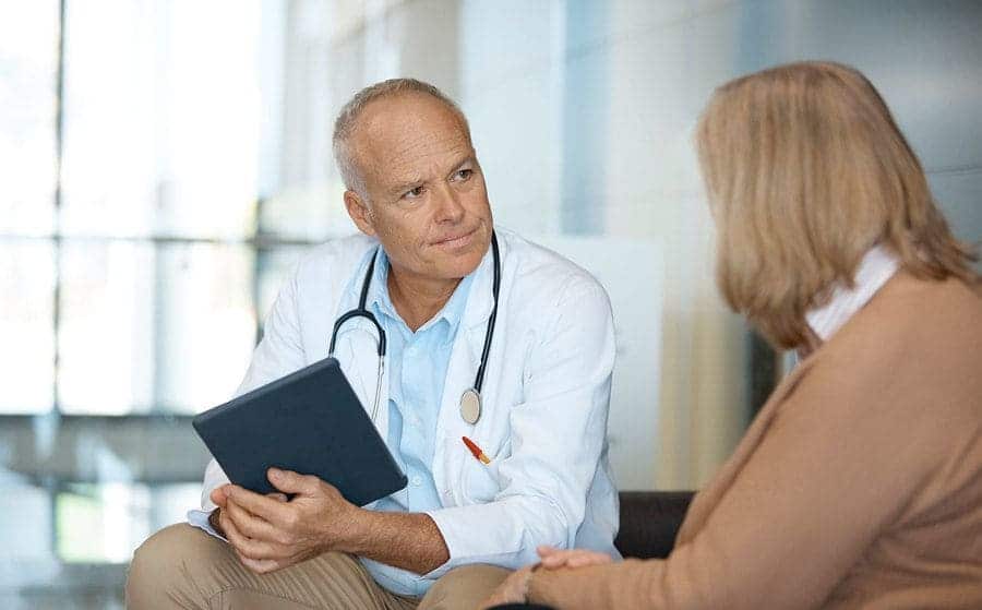 Elderly medical expert is having a meeting with a patient. They are sitting in a hospital.