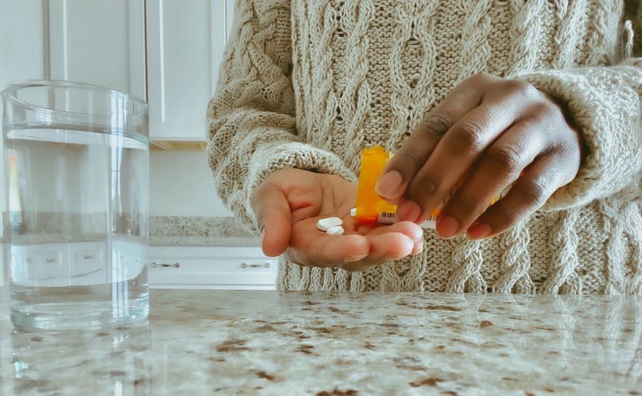 Unrecognizable woman pours pills into a hand from a prescription bottle.