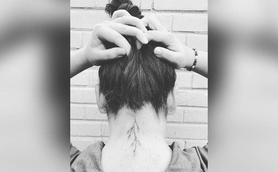 A young girl is showing off her lightning bolt tattoo on the back of her neck. 