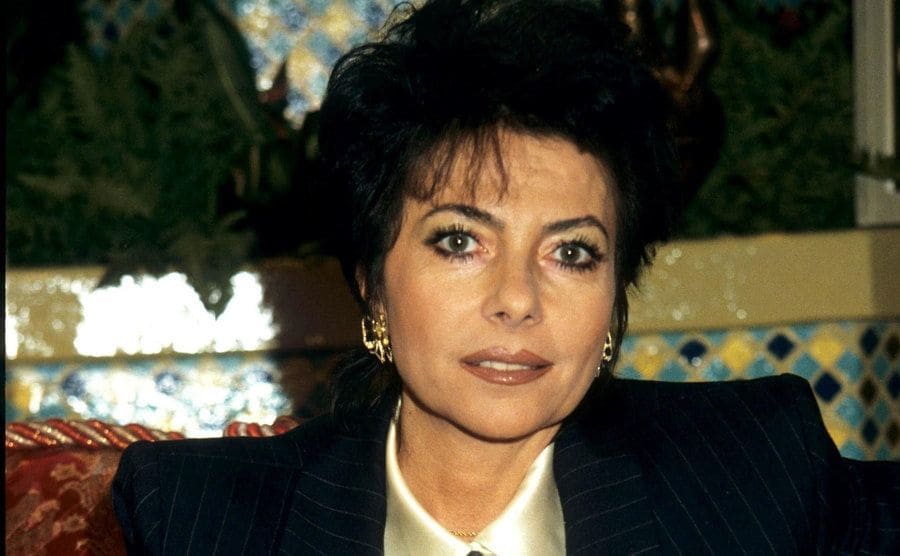 Patrizia Reggiani is sitting on a couch while taking part in an interview. 