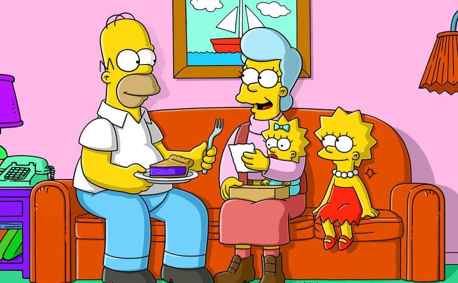 Homer Simpson is sitting on the couch with Glenn Close, Lisa, and Maggie.
