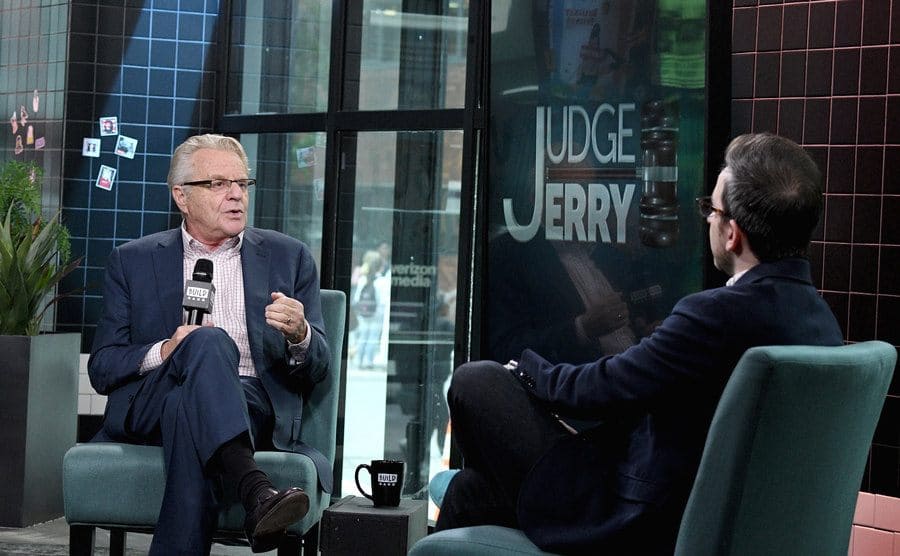 Jerry Springer sitting across from a guest speaking on Judge Jerry