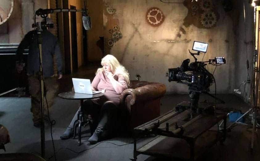 Missy Koski is sitting by her laptop on a TV set.