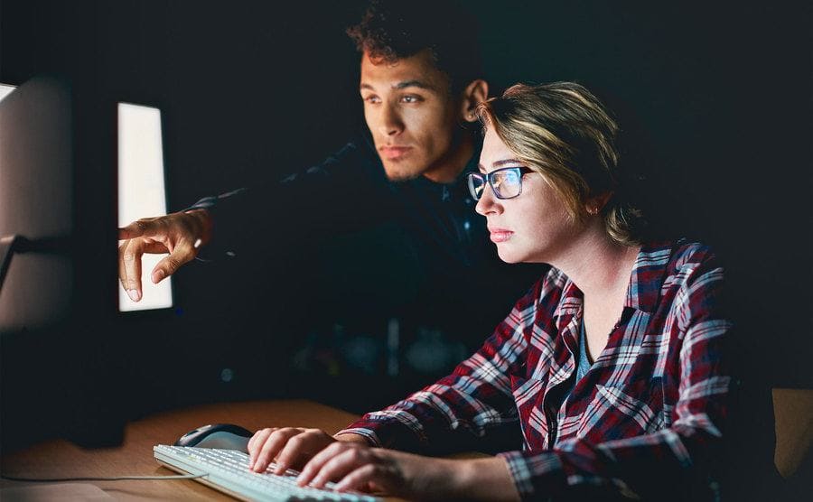 A woman is busy typing on a keyboard as a man points out something on a PC screen to her.