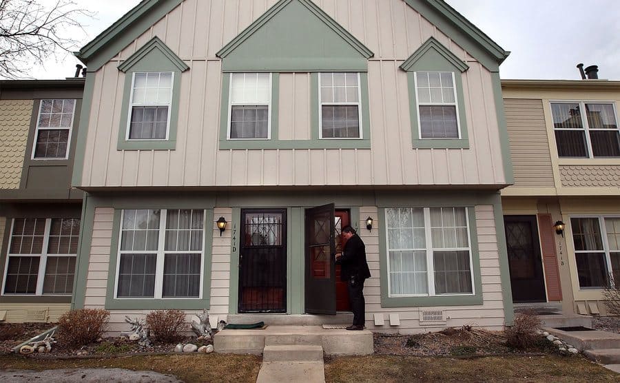 A sheriff officer is standing outside a home on the front steps.