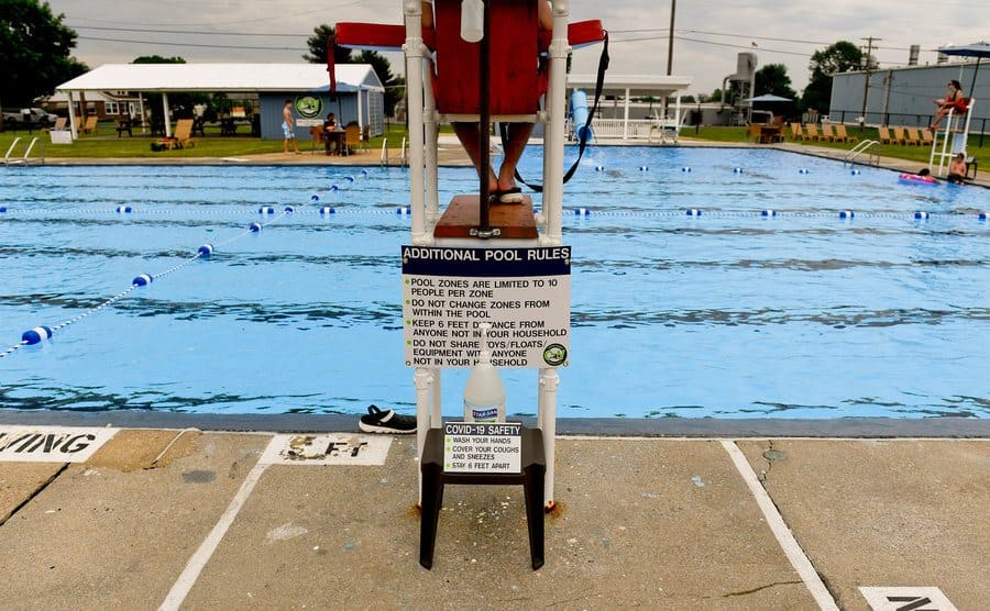A lifeguard is sitting in his chair, looking over the public pool.